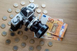 uro banknotes, coins and a camera on a light wooden background.
